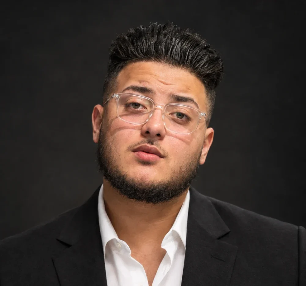 Mohammed Alajnaf, Chief Operating Officer, in a dark suit and white shirt with clear-framed glasses, against a dark background.