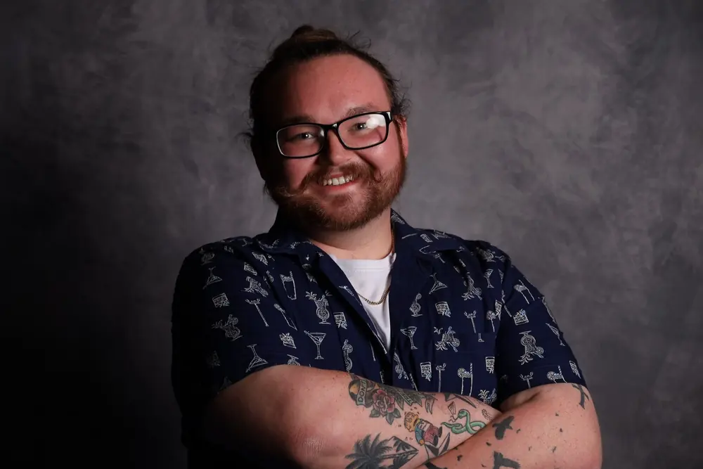 Tobias Waters, a man with glasses and a beard, smiling, against a dark background.